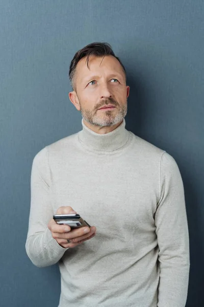 Omtänksamma Mannen Innehar Mobiltelefon Stående Mot Mörk Studio Bakgrund Stirrar — Stockfoto