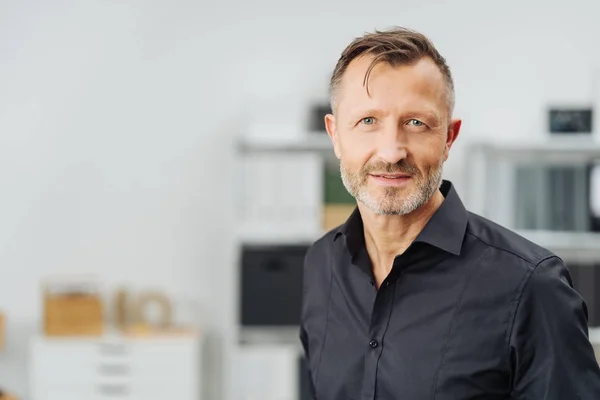 Thoughtful businessman staring into the camera with an intense expression indoors in a spacious office with copy space