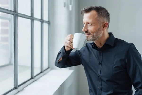 ウィンドウでオフィスでの仕事での休憩中にコーヒーを飲みながら未来について空想自信中年男の肖像 — ストック写真