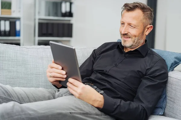 Расслабленный Мужчина Средних Лет Читающий Электронную Книгу Своем Планшете Сидя — стоковое фото