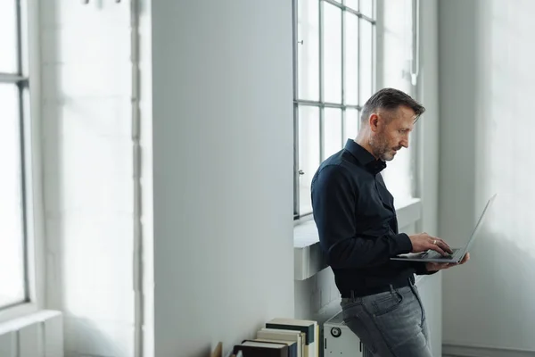 Человек Сидящий Батарее Используя Ноутбук Перед Ярким Окном Белой Комнате — стоковое фото