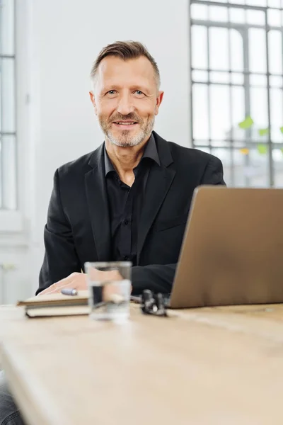 生意人坐在办公室桌上用笔记本电脑微笑在一个低角度视图与前景拷贝空间 — 图库照片
