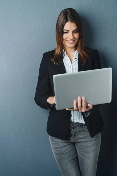 有吸引力的女商人使用手持笔记本电脑 因为她向后靠在一个黑暗的灰色工作室背景 — 图库照片