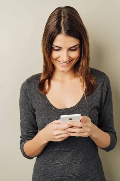 微笑着快乐的年轻女子阅读手机短信对中性演播室背景 — 图库照片
