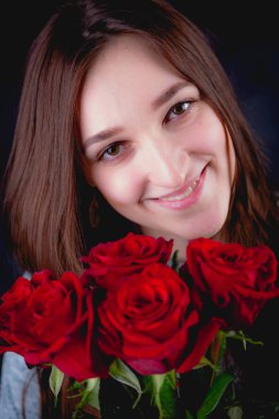 Güzel kız bir buket kırmızı gül, koyu arka plan düzenliyor