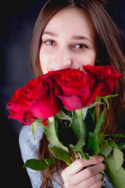 Güzel kız bir buket kırmızı gül, koyu arka plan düzenliyor
