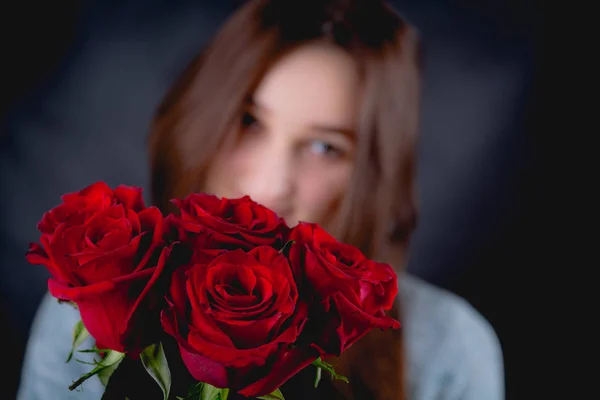 Chica bonita sostiene un ramo de rosas rojas, fondo oscuro — Foto de Stock