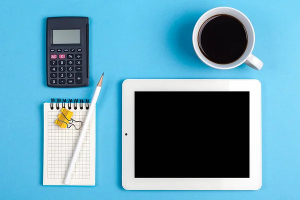 Çalışma alanı üst görünümü. Ofis malzemeleri, kahve, hesap makinesi ve tablet bilgisayarlı bir masa. Üst görünüm mavi arkaplan