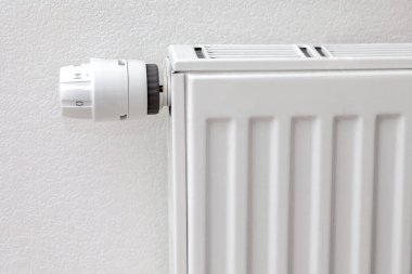 Beyaz radyatörün beyaz ısı kontrol düğmesi. Beyaz bir duvarın önündeki metal radyatör. Roma rakamları