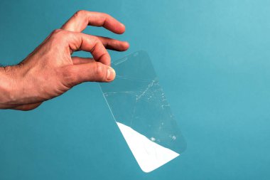 Adam mavi arka planda kırık, kırık bir akıllı telefon güvenlik camını tutuyor. Kırılgan ekipman konsepti