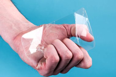 Adamın elinde kırık, kırık bir akıllı telefon camı var. Mavi arka planda. Kırılgan ekipman konsepti