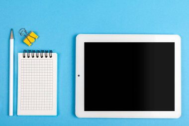 Çalışma alanı üst görünümü. Ofis masasında ofis malzemeleri, hesap makinesi ve tablet bilgisayar var. Üst görünüm mavi arkaplan