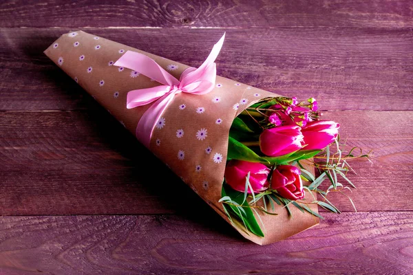 Kraft kağıdında kırmızı ahşap arka planda pembe laleler olan buket.