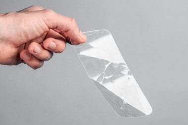 Adam gri arka planda kırık, kırık bir akıllı telefon güvenlik camını tutuyor. Kırılgan ekipman konsepti