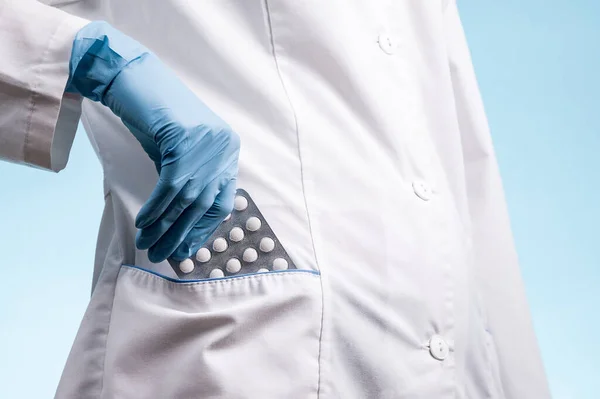 Beyaz önlüklü ve mavi eldivenli doktor sabahlığının cebine bir paket hap koydu.