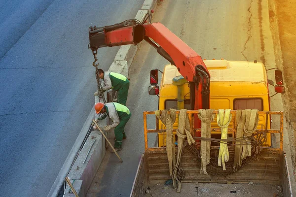 two workers install concrete fence along the road