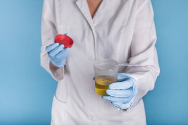 Beyaz üniformalı ve mavi eldivenli bir doktor sarı idrar ve tüplü plastik bir kavanoz tutuyor. Tedavi için idrar içmek