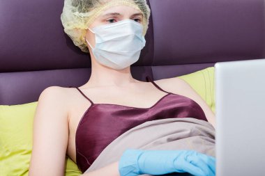 Kendini izole et ve evde covid-19 koronavirüsle çalış. Koruyucu eldivenli bir kız, maske ve saçında bir şapka.