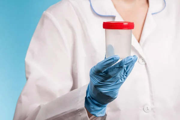 Beyaz üniformalı ve mavi eldivenli bir doktor boş bir plastik test kavanozu tutuyor. Uyuşturucu testi, virüs, hastalık