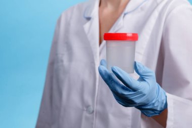 Tıbbi konu: Mavi eldivenli doktorun elinde mavi arka planda idrar analizi için şeffaf bir kap var.