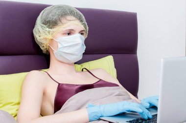 Kendini izole et ve evde covid-19 koronavirüsle çalış. Koruyucu eldivenli bir kız, maske ve saçında bir şapka. Yeni gerçeklik. Normal yaşam ve izole çalışma