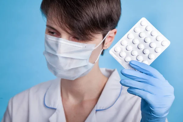 Young attractive female scientist with mask holding a transparent pill with fingers in gloves in the pharmaceutical research laboratory