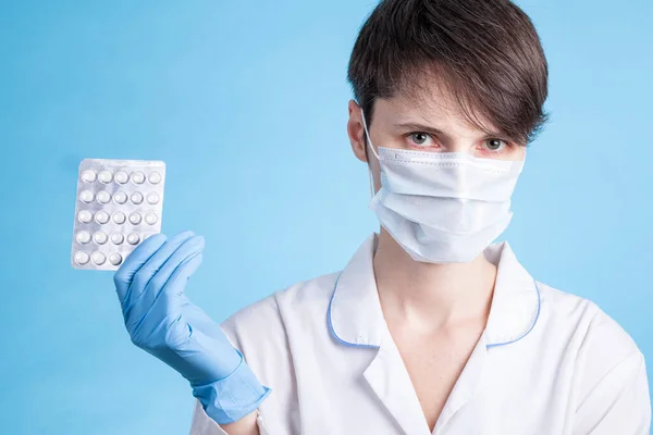 Young attractive female scientist with mask holding a transparent pill with fingers in gloves in the pharmaceutical research laboratory
