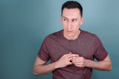 Mavi arka planda genç ve yakışıklı bir adamın portresi. Parmağındaki nişan yüzüğünü aldatma konsepti olarak çıkarmaya çalışıyor.