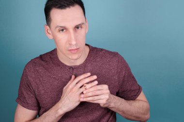 Mavi arka planda genç ve yakışıklı bir adamın portresi. Parmağındaki nişan yüzüğünü aldatma konsepti olarak çıkarmaya çalışıyor.