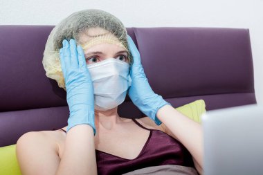 Kendini izole et ve evde covid-19 koronavirüsle çalış. Koruyucu eldivenli bir kız, maske ve saçında bir şapka. Yeni gerçeklik. Normal yaşam ve izole çalışma