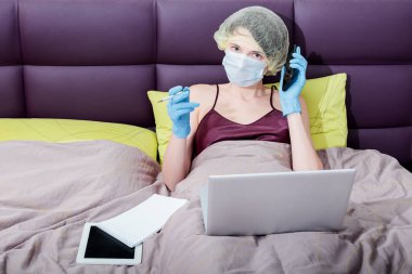 Kendini izole et ve evde covid-19 koronavirüsle çalış. Koruyucu eldivenli bir kız, maske ve saçında bir şapka. Yeni gerçeklik. Normal yaşam ve izole çalışma