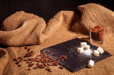 Çuval bezinin üstünde şeffaf cam bir fincanda sade kahve. Şekerin, kahve çekirdeğinin ve öğütülmüş kahvenin yanında. Vintage