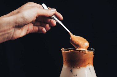 Kız, buzlu Kore Dalgona Kahvesi 'ni bir kaşıkla karıştırıyor. Moda kremalı kremalı ve buzlu kahve. Moda kahve içeceği.