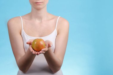 Mavi arka plandaki genç kız, sağlıklı beslenme ve vejetaryenlik kavramı olarak elinde güzel bir elma tutuyor.