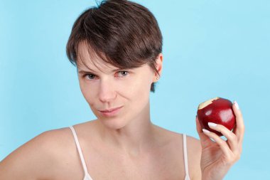 Mavi arka plandaki tatlı kız kırmızı elmayı ısırıyor. Vitaminlerin ve sağlıklı beslenmenin faydaları