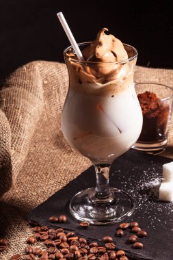 Dalgona kahvesi, köpüklü sütlü soğuk içecek, hazır kahve, Kore modası ev yapımı kahve. Siyah bir taş standında şeker ve kahve çekirdeğinin yanında duruyor.