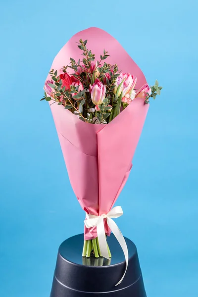 bouquet of flowers with tulips in pink packaging on a blue background. close-up, high quality.