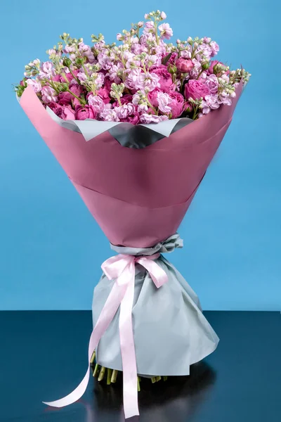 stock image bouquet of flowers with roses and Mattioli in pink packaging with a blue background. high quality.