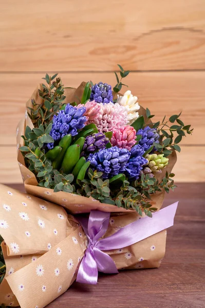 bouquet of flowers with multi-colored hyacinths in a craft paper package on a wooden background. high quality.