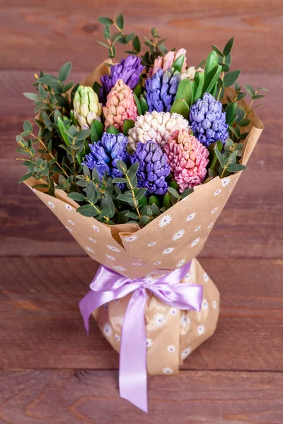 bouquet of flowers with multi-colored hyacinths in a craft paper package on wooden background. high quality.