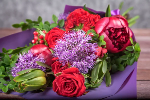 bouquet with red flowers in purple packaging on a wooden background. high quality