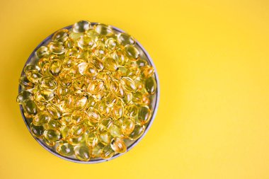 Sarı arka planda duran Omega 3 kapsülleri. Haplı balık yağı. Sağlık desteği ve tedavi. Biyolojik olarak aktif katkı maddeleri. Seçici odaklanma. Kapat, üst görünüm, yüksek çözünürlüklü ürün.