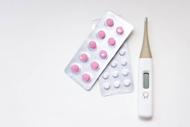 Renkli antibiyotik kapsül hapları. Kabarcık paketinde pembe ve beyaz renkli ve beyaz arka planda termometre. Eczane arka planı ve dijital termometre. - Yakın çekim. Boşluğu kopyala.