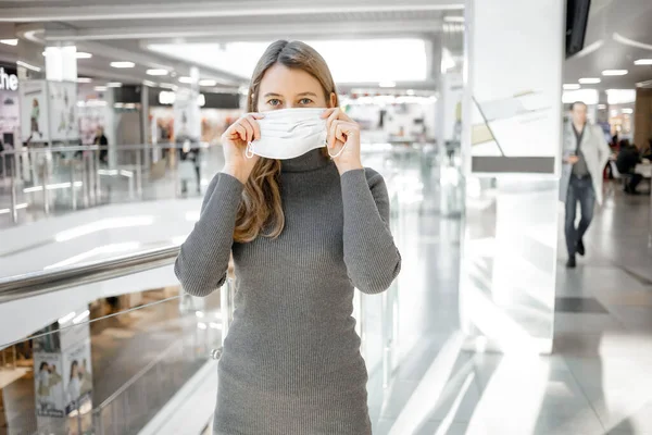 Girl with medical mask to protect her from virus. Coronavirus pandemic. Woman with mask standing in Mall. People being hospitalized, often put in quarantine (isolation) to stop spreading Corona.