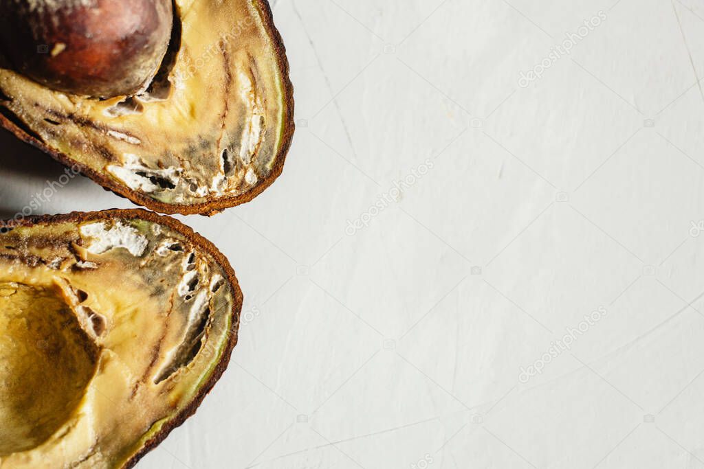 Rotten spoiled overripe avocado fruit cut in half on grey background. Stop wasting food. Close up. Copy space.