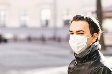 Koruyucu maskeli bir adam karantina şehrinde yürüyor. Yüzünde tıbbi maske olan bir adam kameraya bakıyor. Coronavirus. Virüs koruması. Hastalık salgını.