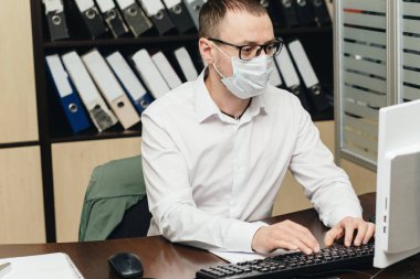 Ofisteki işçiler koruyucu maske takarak bilgisayar başında çalışıyor. Coronavirus için karantinada bir şirket var. COVID-19 Pandemik Coronavirüs.