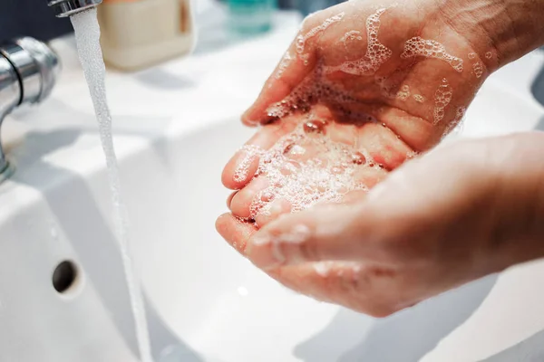 Male in bathroom washing his hands. A man draws water in the palm of his hand to wash off soap foam from the hands of his hands. Close up. Protection from coronovirus