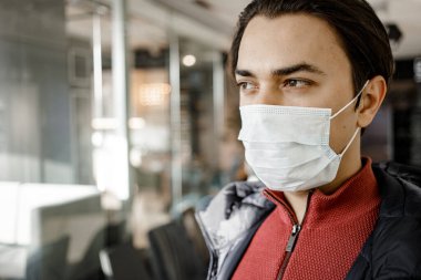 COVID-19 Pandemic Coronavirus Genç adam NCov 2019 'dan korunmak için koruyucu yüz maskesi takıyor. Cerrahi steril maskeli yakışıklı adama yaklaş. Karantina ve sağlık konsepti. Boşluğu kopyala.