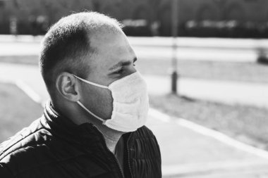 Sokakta tıbbi maske takan hasta bir genci kapatın. Virüslere karşı koruma, enfeksiyon, egzoz dumanı. Hastalık kavramı. Corona virüsü. Siyah beyaz görüntü. Boşluğu kopyala.